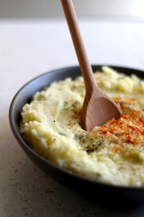 Bowl of mashed potatoes seasoned with onion, parmesan and smoked pepper. Selective focus.