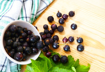Fresh ripe black currants berries. Blackcurrant fruit in white bowl with green leaves on wooden background.  Summer healthy food. Juicy natural fruit. Close up, selective focus.