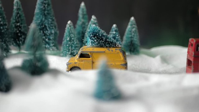 Winter forest miniature with a small yellow toy car with a Christmas tree on the roof, double-decker red bus, snowdrifts and Christmas trees.