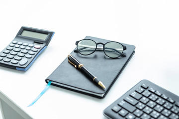 Close-up of business working equipment of glasses and pen on notebook, keyboard and calculator on White wooden table background in office top view copy space,Office tools