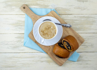 Cup of coffee and poppy seed buns on a wooden Board. Composition with a Cup of coffee and buns on the white wooden kitchen table. Concept lifestyle. Flat lay.