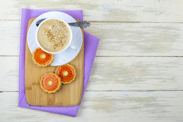 Cup of coffee and sweet cookies with orange jelly on wooden Board. Composition with Cup of coffee and sweet cookie glazed with jelly flavored orange on wooden kitchen table with copy space.