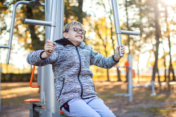 Obraz premium Smart kid boy does workout on trainer equipment outdoor. Children, sport, activity and healthcare concept