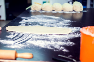 A woman rolls out the doughon on black table.