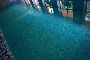 Reflection of windows and lamps of an indoor swimming pool in a smooth surface of the water, background