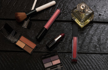 Various cosmetics on a black background (nail polish, eye shadow palette, lipstick, brush, parfume). Close up photo.