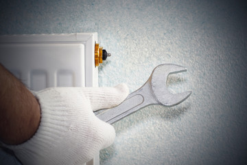Man is repairing radiator battery in the room. Maintenance repair works renovation in the flat. Heating restoration. Wrench in hands