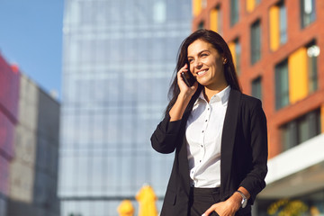 Hispanic businesswoman smiling speaks on a mobile outdoors