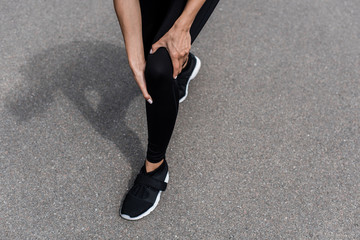 cropped view of sportswoman in black sneakers with knee pain on street