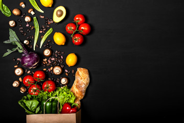 Shopping paper bag full of different fresh vegetables and bread on a black background. Purchases concept. Healthy food organic selection. Top view, copy space.