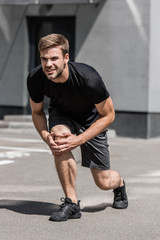 bearded sportsman in black t-shirt with knee pain on street