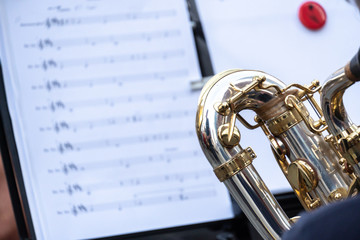 Cropped image of a back turned saxophone player. In the background, an out of focus score