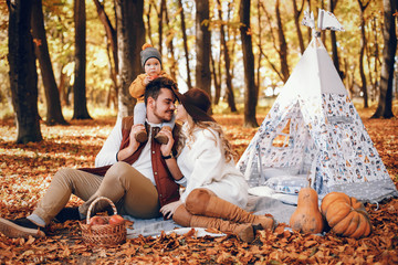 Family have fun in a autumn park. Cute blode in a white sweater. Parents with little son. Family sitting near wigwam;