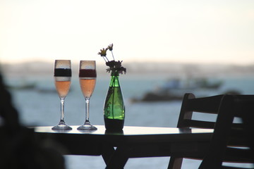 Two glasses of sparkling rose wine and a green bottle with flower on wooden table
