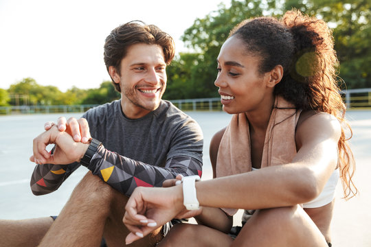 Photo of attractive smiling couple sitting and using smartwatch