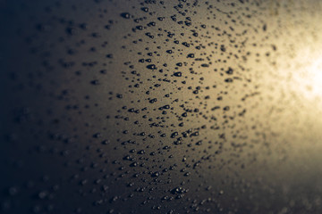 Water drops on the rough surface in the rays of the evening sun background texture