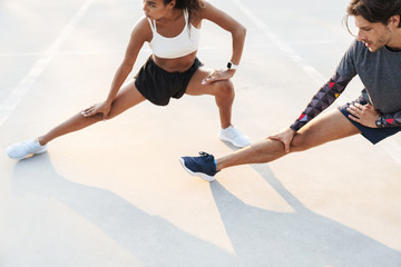 Photo of strong multinational couple stretching their legs together