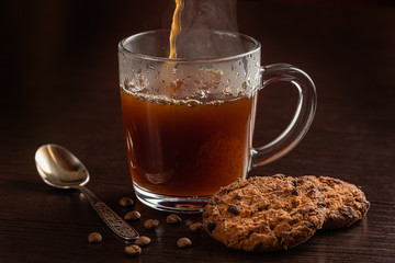 a hot drink fills the Cup. oatmeal cookies lie on a wooden table nearby. horizontal Studio photography on a dark background
