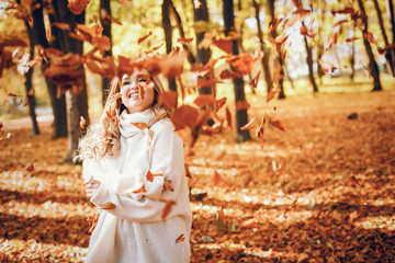 Beautiful girl in a autumn park. Cute blode in a white sweater.