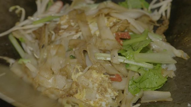 An extreme closeup shot of freshly saut�ed rice noodles, sliced pork, and mixed vegetables being served on a polystyrene box in a street food stall.