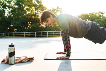 Photo of young caucasian man doing exercise on mat while working