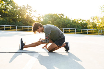 Photo of young caucasian man stretching his leg on mat