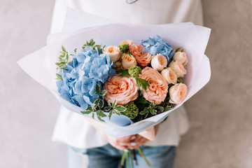 Very nice young woman holding a beautiful blossoming flower bouquet of fresh hydrangea, roses, carnations in pink and light blue colours on the grey wall background 