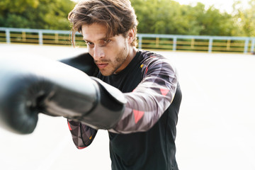 Photo of strong masculine man doing workout in boxing gloves