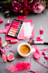 Obraz na płótnie Canvas Make up artist essentials: pink lipstick palette, eye shadows, lipsticks, flower petals, espresso coffee cup and floral bouquet on the background in pink colors 