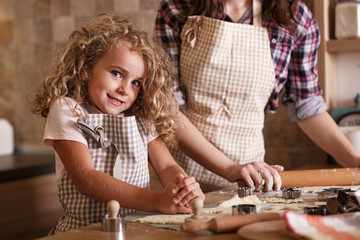 Little curly hair girl making cakes with her mother in kitchen.