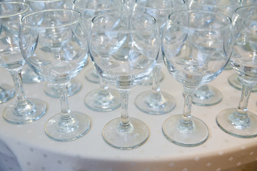 Empty clean glasses standing in a row on a table prepared by the bartender for champagne and wine. Several of transparent glasses on a rack. Catering for the event. A lot of wine glasses in a row .