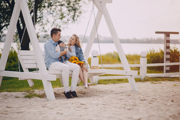 beautiful long-haired blonde with her handsome man and small newborn son sitting on the swing with sunflowers