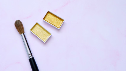 Paint brush and golden color palettes, with pink background.