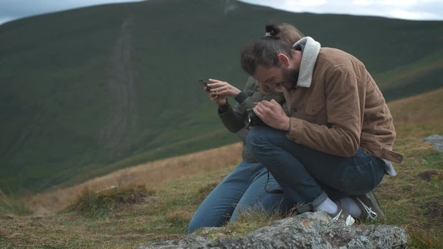 Two travelers take a photo on a smartphone and a camera in the mountains.