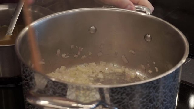 Onion and garlic with rosemary frying in the soucepan. Hands stirring vegetables with spatula. Closeup shot