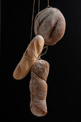 Fresh bread of various shapes hanging on the ropes on a black background.
