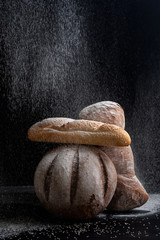Fresh bread under a pouring flour on a black background..