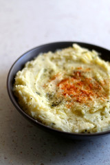 Bowl of mashed potatoes seasoned with onion, parmesan and smoked pepper. Selective focus.