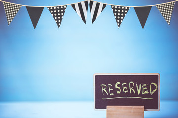 reserved text on wooden blackboard with decorated flag over blue wall background.