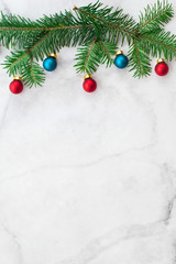Fir-tree branches decorated with red and blue balls on gray marble background. New Year, Christmas and winter concept. Flat lay, top view, free copy space.
