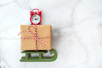 Christmas gift wrapped in brown craft paper and clock on wooden sleigh Christmas toys on gray marble background. New Year, Christmas and winter concept. Flat lay, top view.