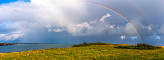 Moody sky with full rainbow bridge on british coast, South Wales, Uk. - obrazy, fototapety, plakaty