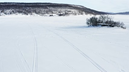 Sweden, drone flying sunny winter day over frozen lake and small island with small mountain birches in  Northern Sweden. Breathtaking view over Scandinavian Mountains