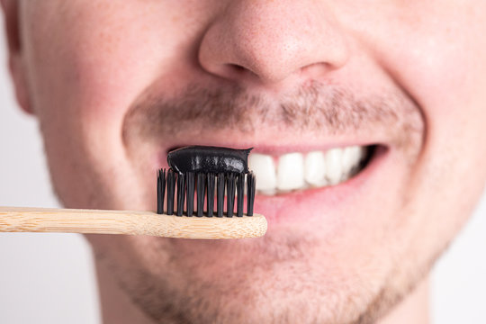 a man brushes his teeth with a black whitening toothpaste with the addition of coal, a bamboo ecological toothbrush.