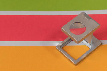 Silver magnifying glass standing on  the test print, colored background. Print loupe on offset...