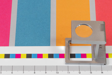 Silver magnifying glass standing on  the test print, colored background. Print loupe on offset...