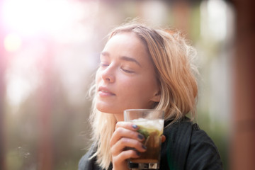 Attractive woman in her 20s with a glass cocktail or ice tea outside in sunlight