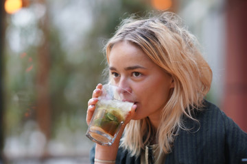 Attractive woman in her 20s with a glass cocktail or ice tea outside in sunlight