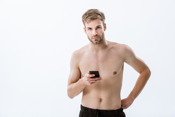 Fototapeta premium bearded shirtless sportsman looking at camera and holding smartphone isolated on grey