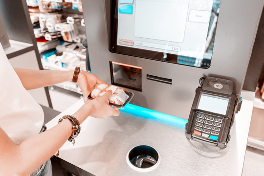 The girl in the supermarket buys sushi and makes a purchase at the checkout self-service